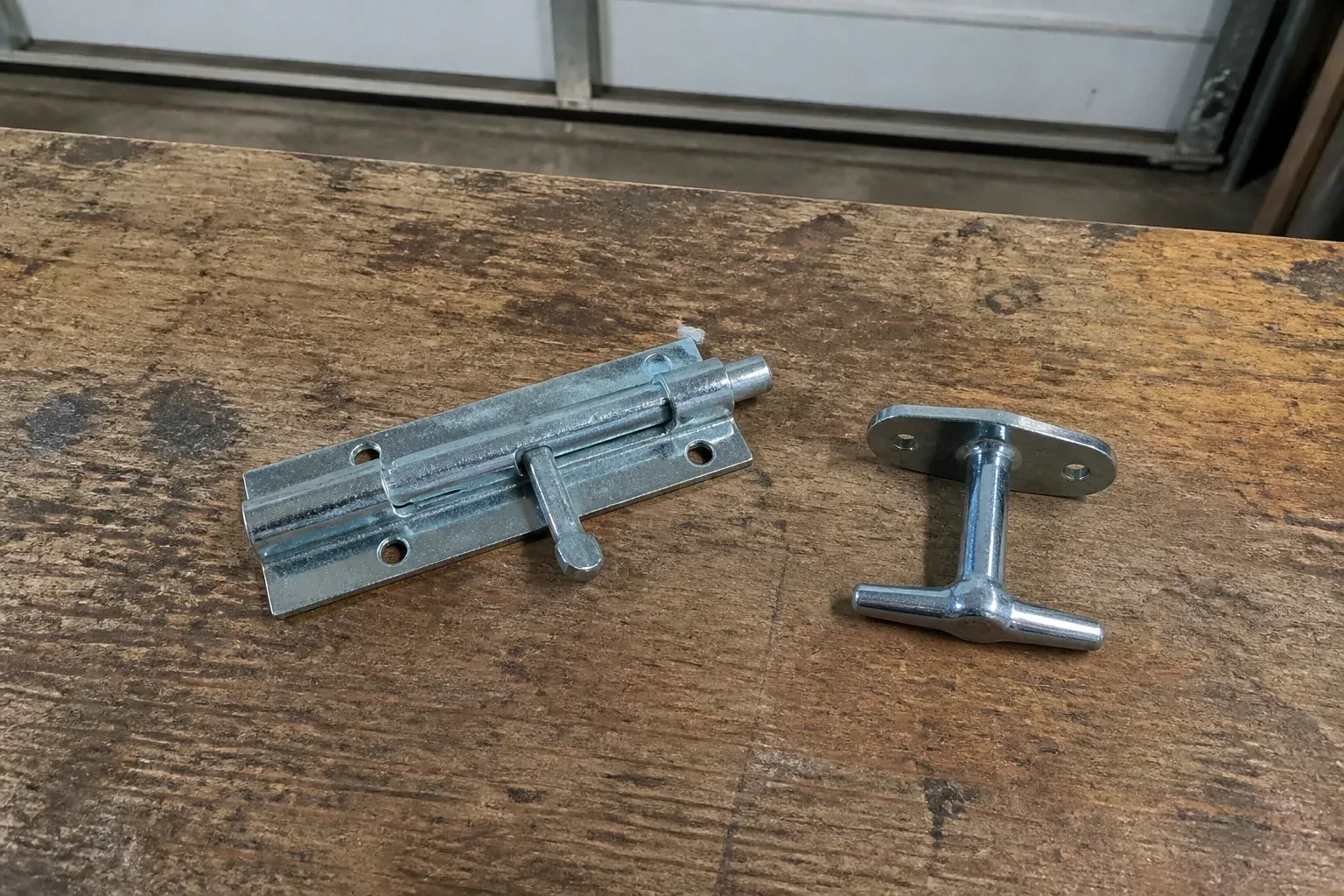 Detached slide bolt and T-handle on a wooden garage workbench. — Garage Door Manual Lock Repair, Mississauga